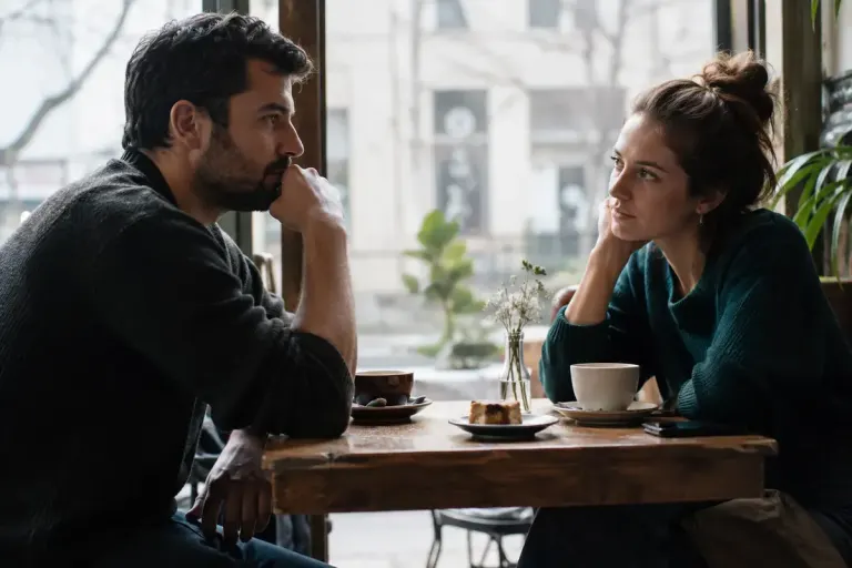 Two adults in a quiet reflective conversation across a small cafe table.
